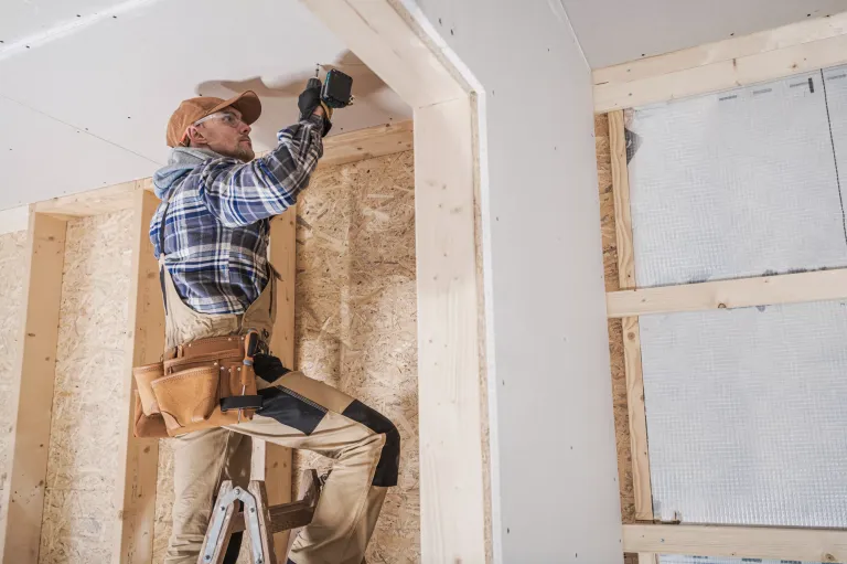 General Construction Contractor Attaching Drywall Using Cordless Drill Driver. Caucasian Remodeling Worker in His 40s.
