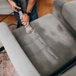 Handsome zoung man cleaning furniture. Process of deep furniture cleaning, removing dirt from sofa. Washing concept.